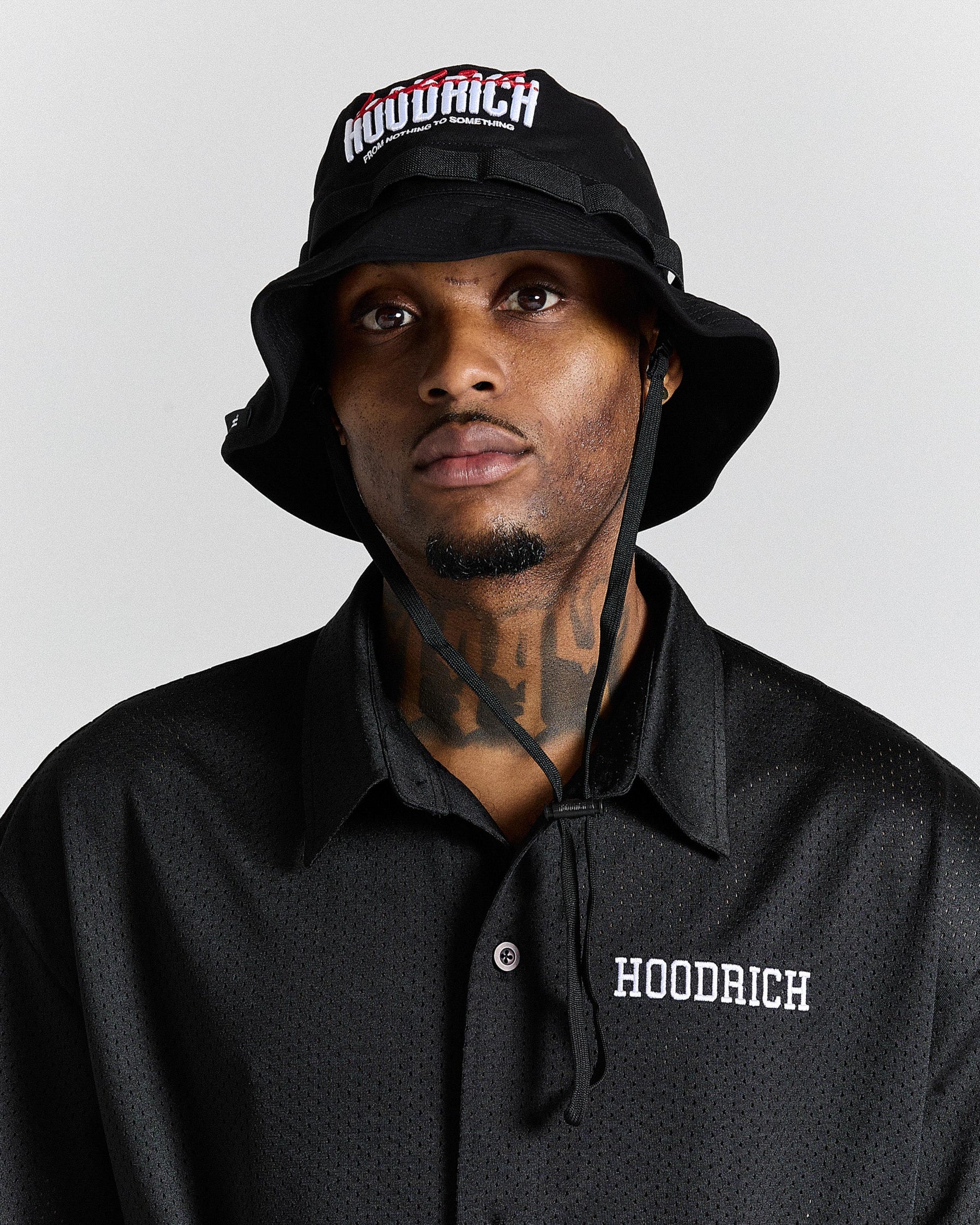 Person wearing a black 'Hoodrich' bucket hat and shirt against a gray background