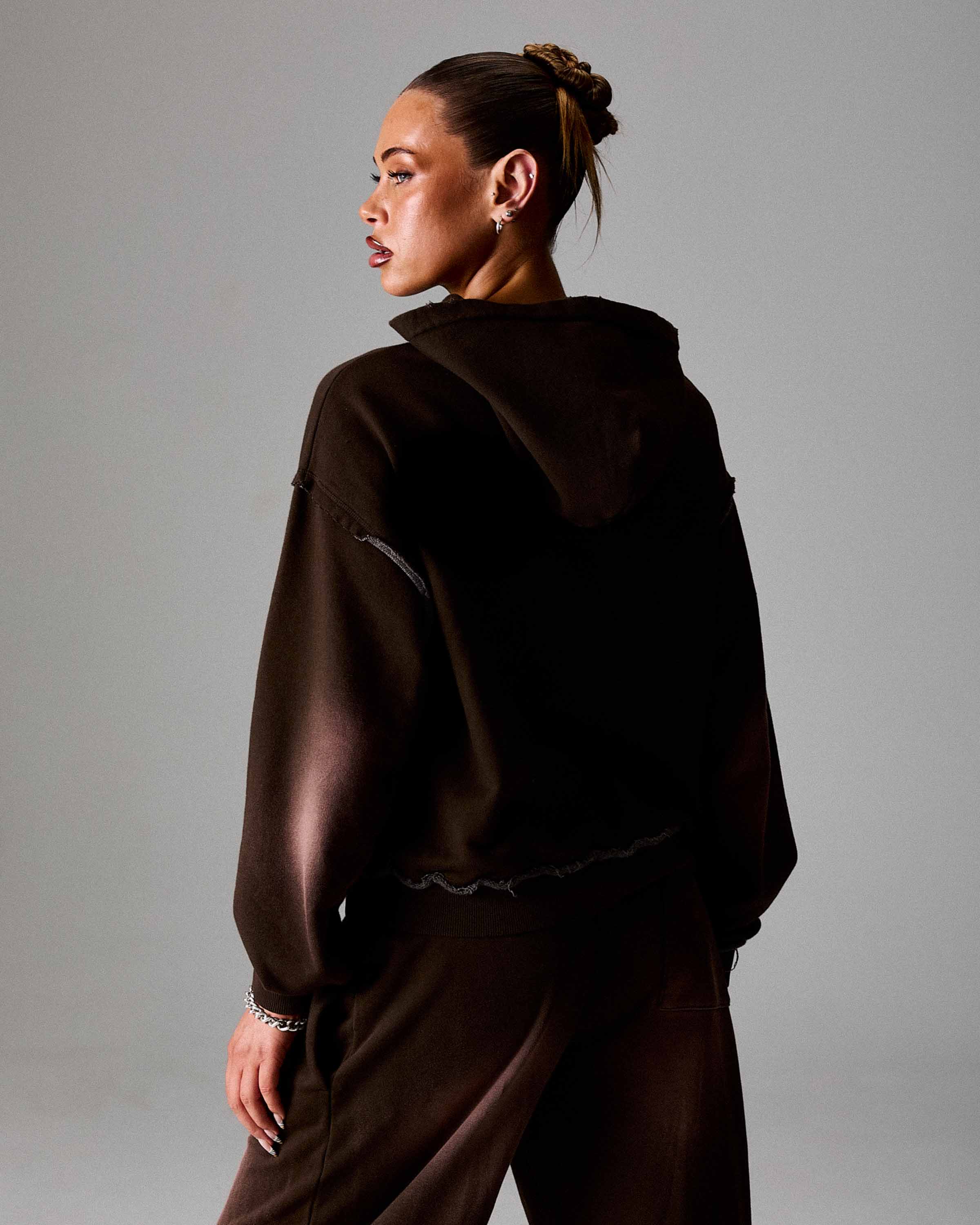 Person wearing a dark brown hoodie and pants against a gray background