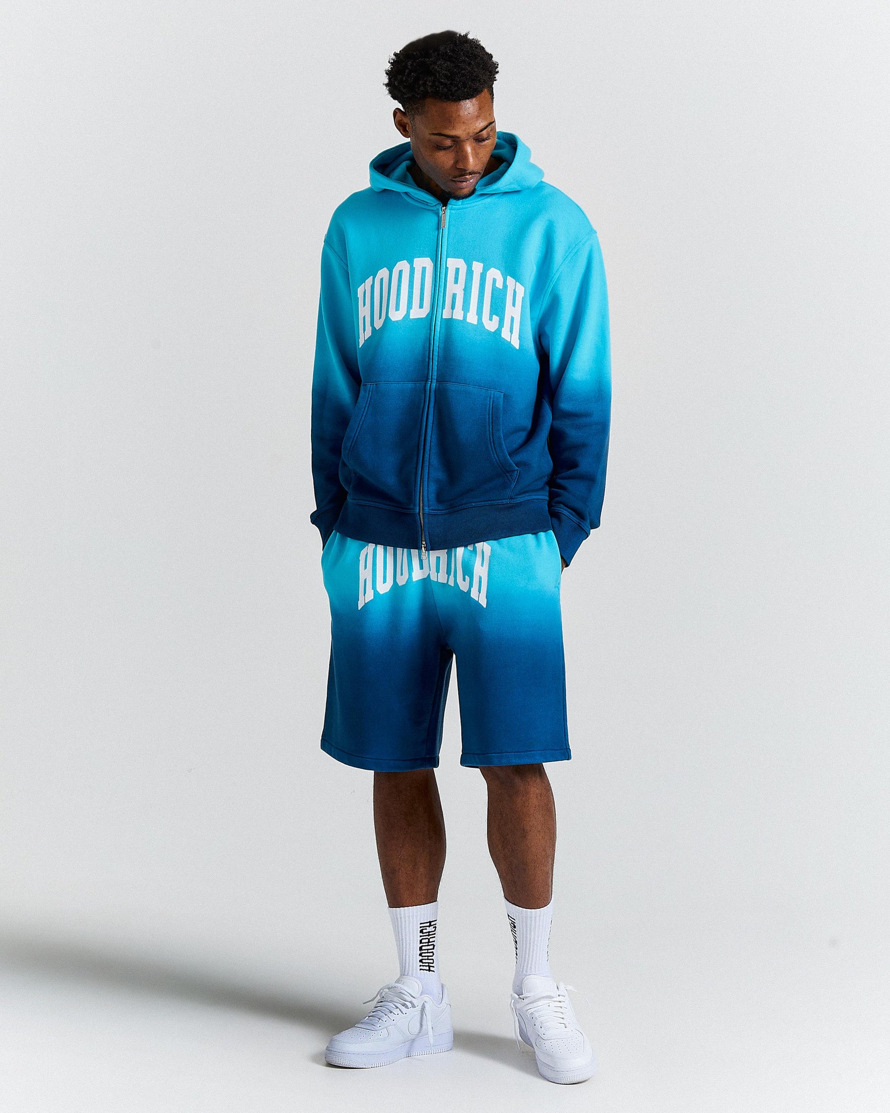 Person wearing a blue 'Hood Rich' hoodie and shorts set on a white background