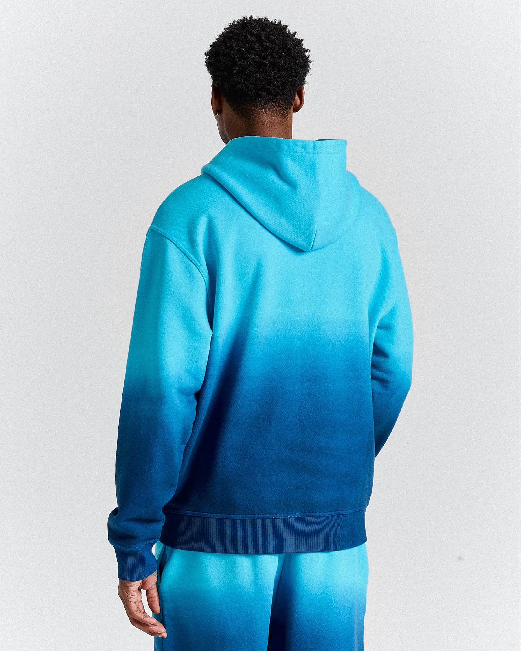 Person wearing a blue ombre hoodie on a light gray background