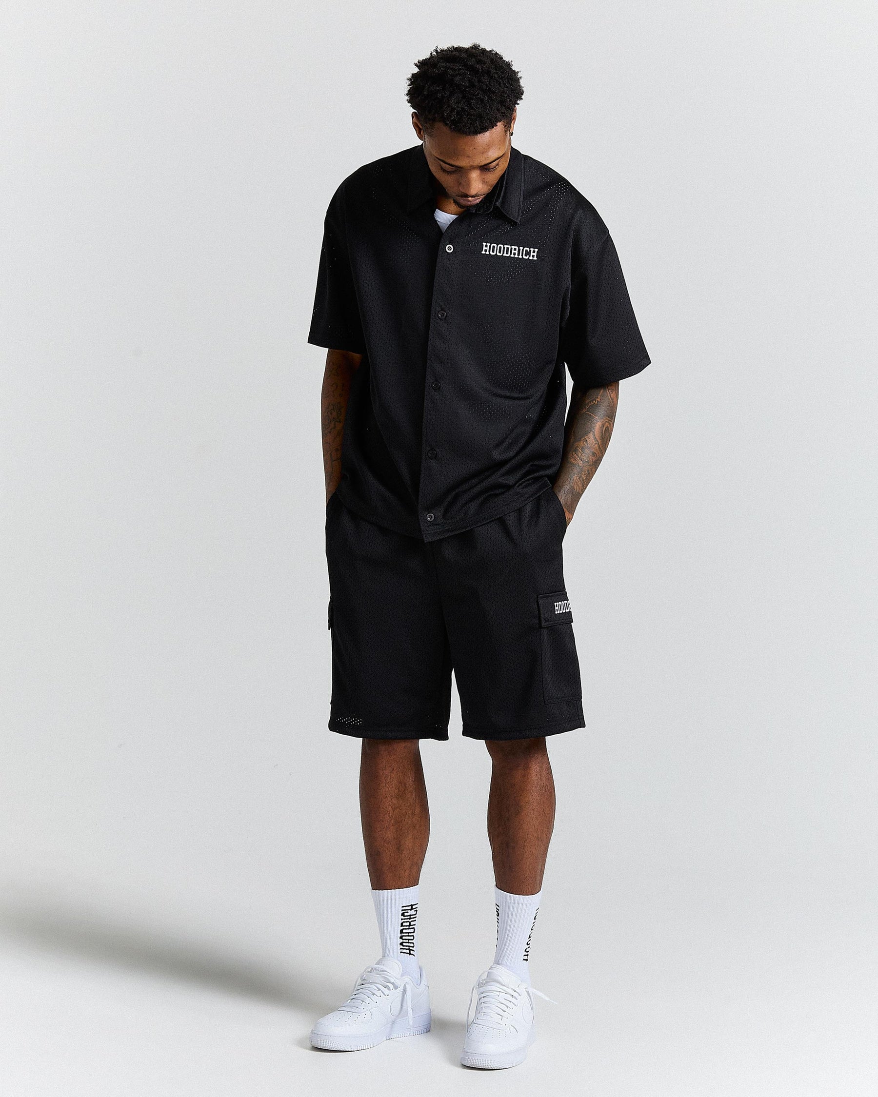 Person wearing a black shirt and shorts with visible branding on a light gray background