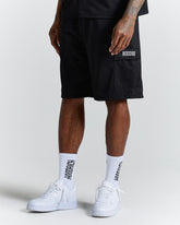 Person wearing black shorts with a brand logo, white socks, and white sneakers on a light gray background