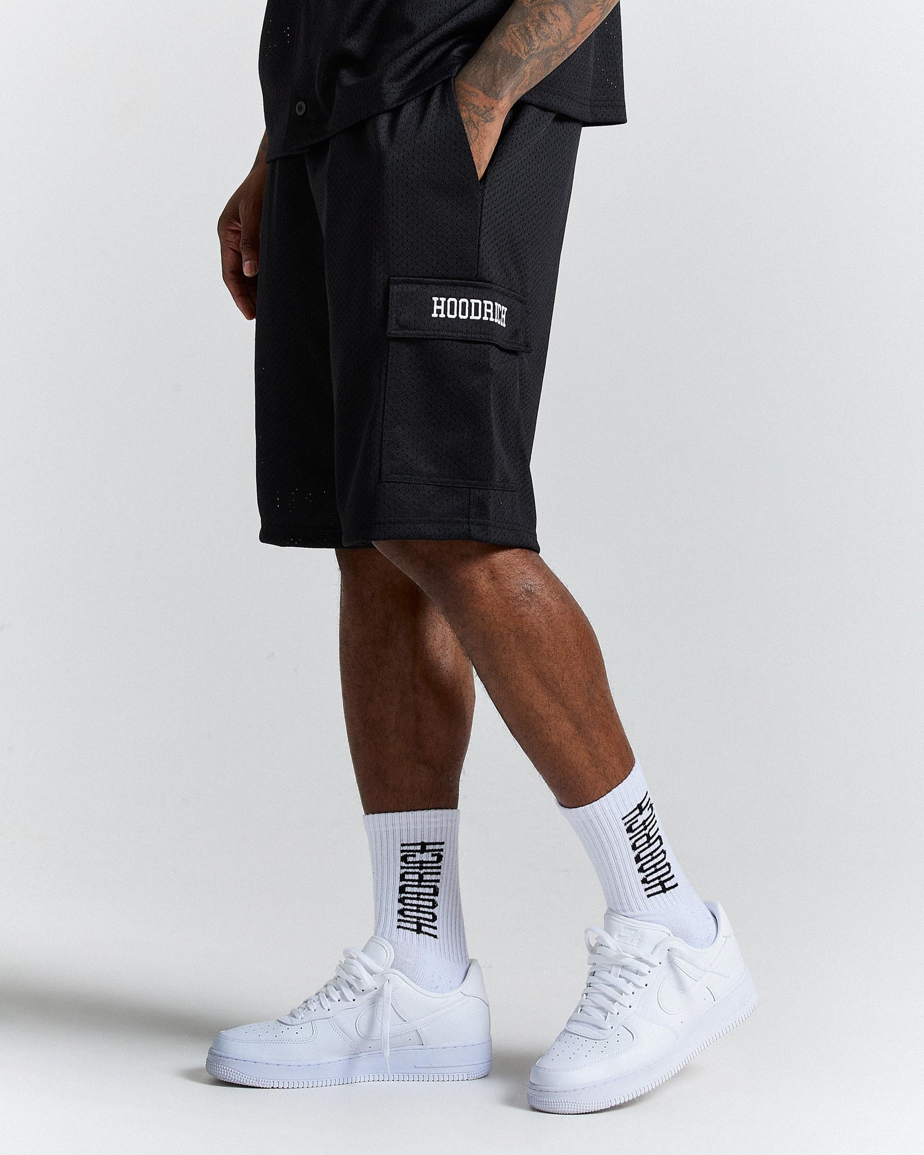 Person wearing black shorts with 'Hoodie' branding, white sneakers, and socks on a light gray background