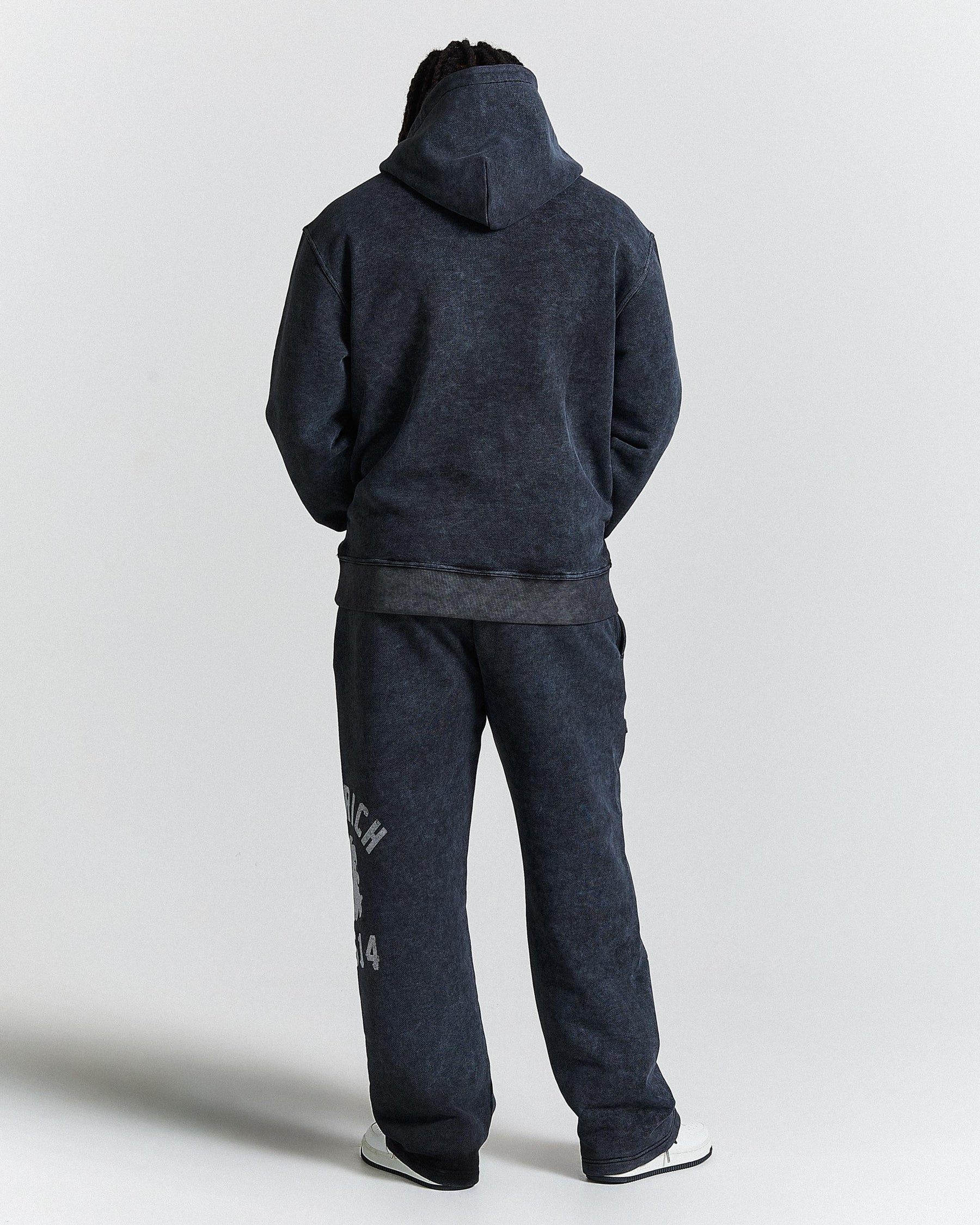 Person wearing a dark gray hoodie and pants on a light gray background