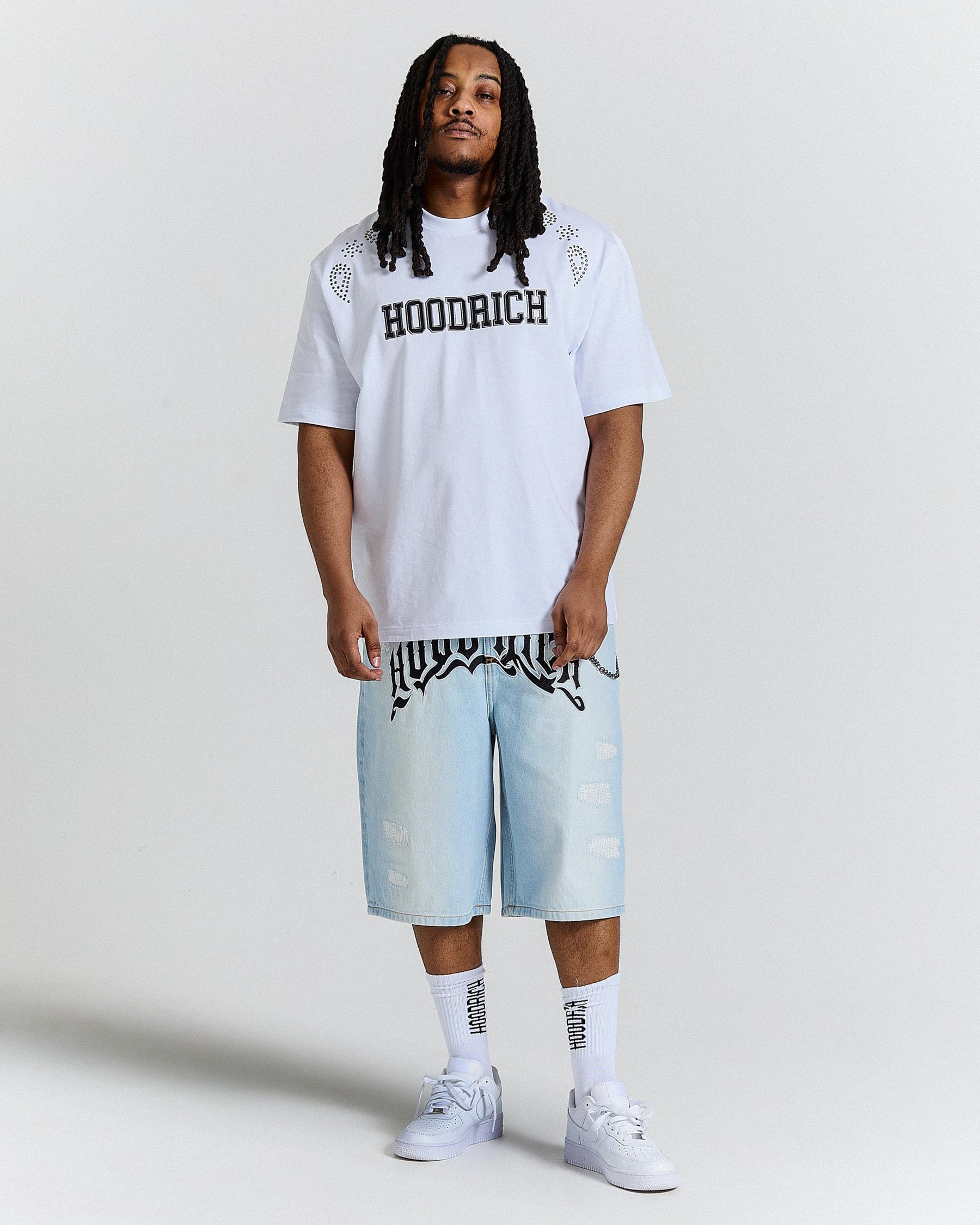 Person wearing a white 'Hoodrich' t-shirt and light blue shorts on a plain background